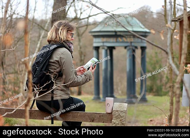 29 March 2023, Saxony-Anhalt, Alexisbad: A hiker sits on a bench with a hiking booklet of the Harzer Wandernadel in the Selketal Stieg