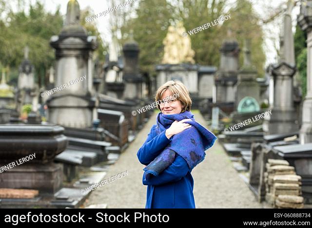 Portrait of a thirty year old woman with a blue winter coat and scarf at a cemetery