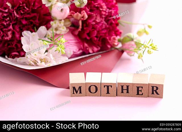 A bouquet of flowers and a block of text for mother placed on a pink background. Mother's Day image