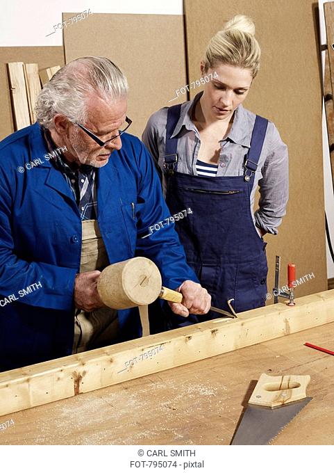A man demonstrating wood chiseling to a woman in a workshop