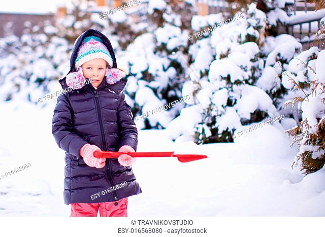 Little girl playing with red shovel in the garden