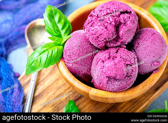 Artisanal blueberry ice cream with green basil in a wooden bowl close-up, selective focus. Top view