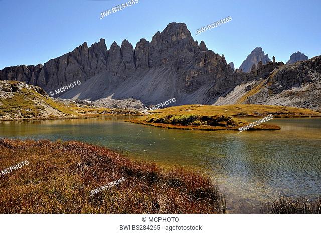 jagged backlit east ridge of Monte Paterno seen across a lake, Italy, Dolomites, NP Sesto Dolomites