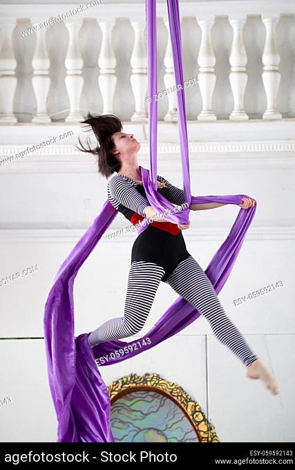 Young woman air gymnast flying on aerial silk in a studio