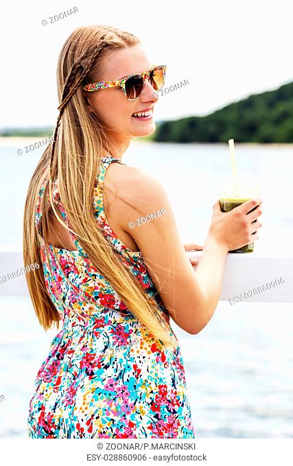 Beautiful young woman with sunglasses drinking green vegetable smoothie