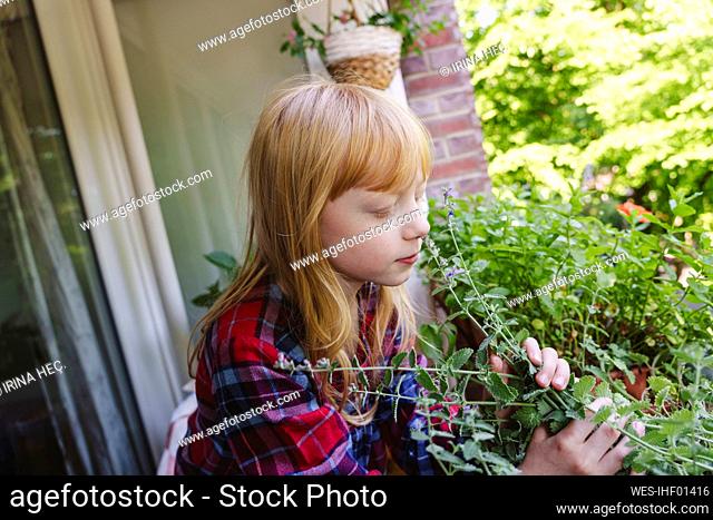 Blond girl smelling plant in balcony