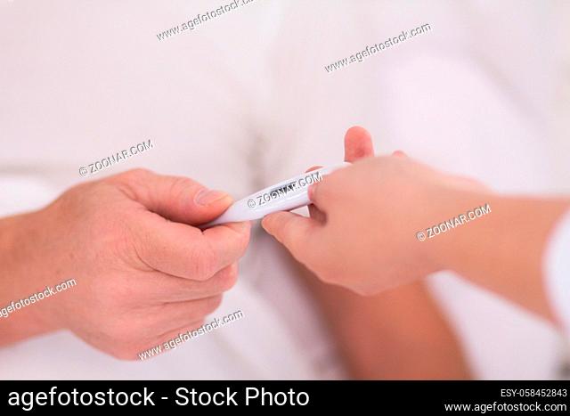 Close up picture of thermometer being passes to another person. Close up shot of nurses hand handing thermometer to her aged patient