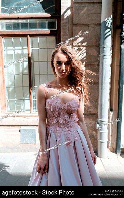 Young beautiful woman model in a stylish evening dress posing on a background of the city on the balcony of an old building