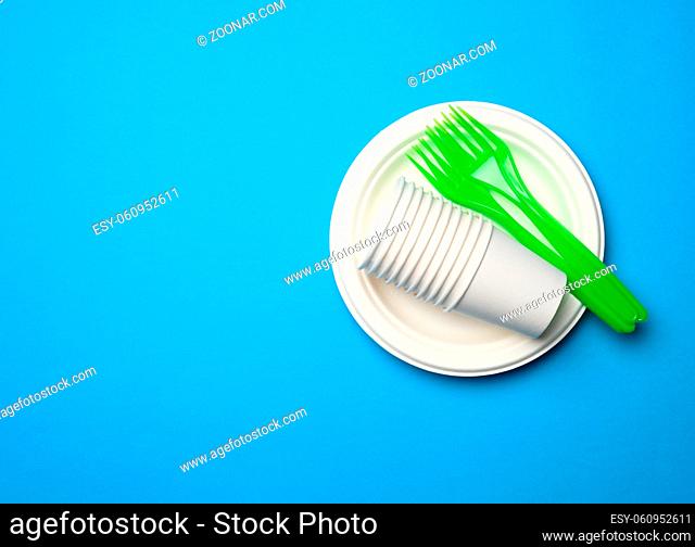 green plastic forks and empty white paper disposable plates on a blue background, top view, set