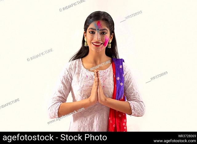 A YOUNG WOMAN WITH GULAL ON HER FACE GREETING WITH FOLDED HANDS