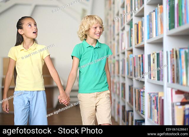 Surprised teenage girl and a smiling boy staring at the shelving units in the library