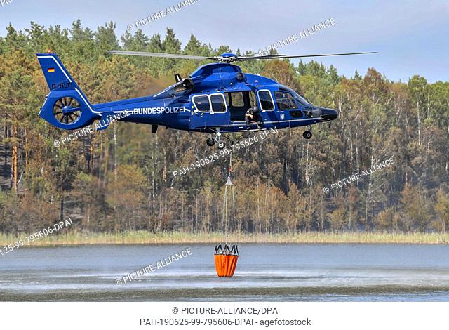 25 June 2019, Brandenburg, Lieberose: A helicopter of the federal police picks up water in the tar furnace lake to fight the forest fire in the Lieberoser Heide