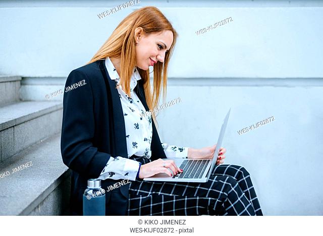 Young businesswoman sitting on stairs using laptop