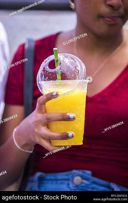 An African teenage girl drinks a cold frozen slushee drink at the county fair in Arlington, Virginia
