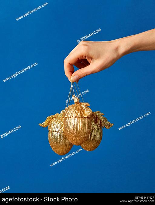 Christmas decoration golden acorns in a woman hand on a classic blue background with copy space