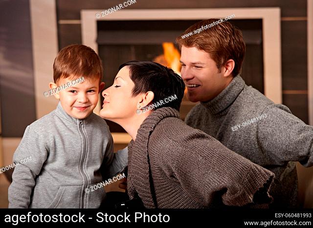 Happy family sitting on couch at home in front of fireplace, looking at camera, smiling