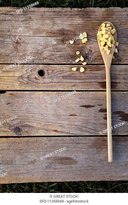 A wooden spoon with sweetcorn on a wooden surface