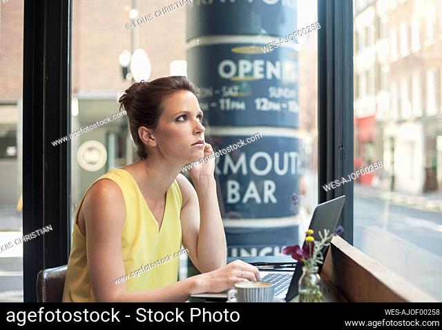 Thoughtful young businesswoman with laptop at coffee shop