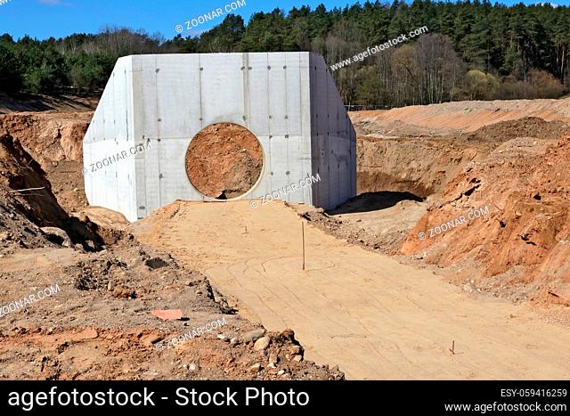Large concrete collector for sewer pipes and heaps of sand with traces of heavy equipment wheels on a construction site in the forest