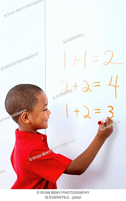 Boy writing answers to sums on whiteboard