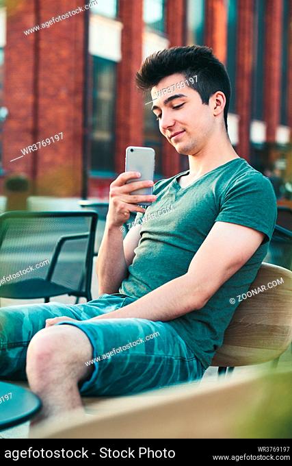 Young man having fun with smartphone, capturing photo, sitting in center of town