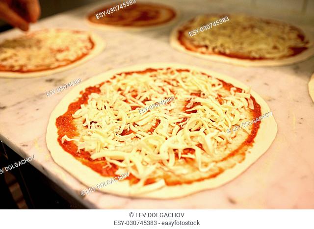 food, culinary, italian cuisine and cooking concept - raw pizza with grated cheese on table at pizzeria