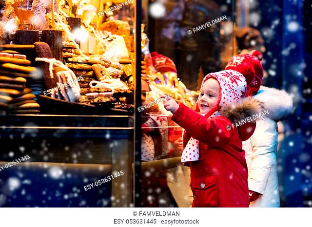 Children window shopping on traditional Christmas market in Germany on snowy winter day. Kids buying candy, pastry and gingerbread in confectionery