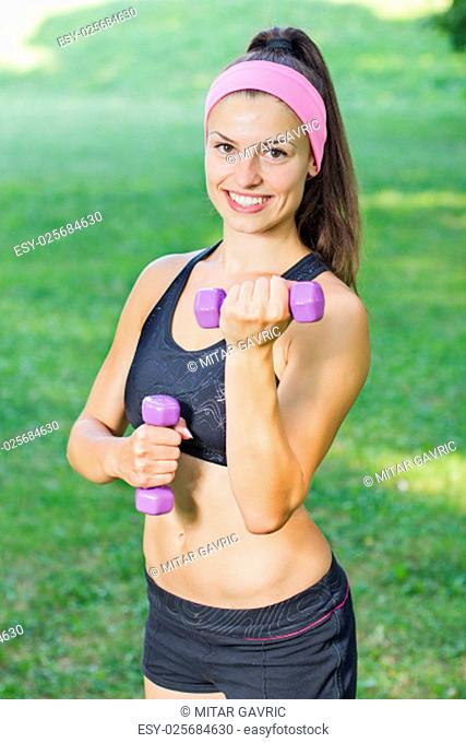 Fitness Slim Woman Training with dumbbells. Smiling attractive female practicing using hand weights outdoor. Healthy lifestyle workout concept on beautiful...