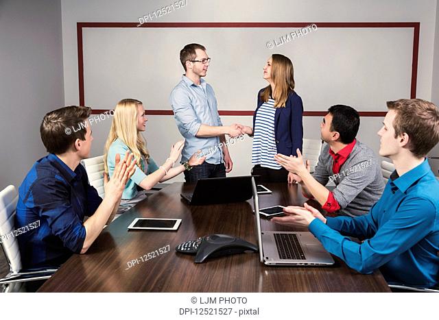 Young millennial business professionals working together in a conference room in a place of business and praising the efforts of one of their peers; Sherwood...