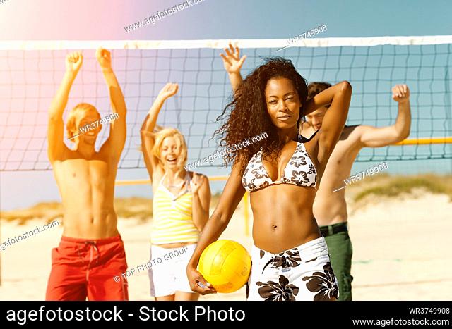 Group of friends - women and men - playing beach volleyball, one in front having the ball