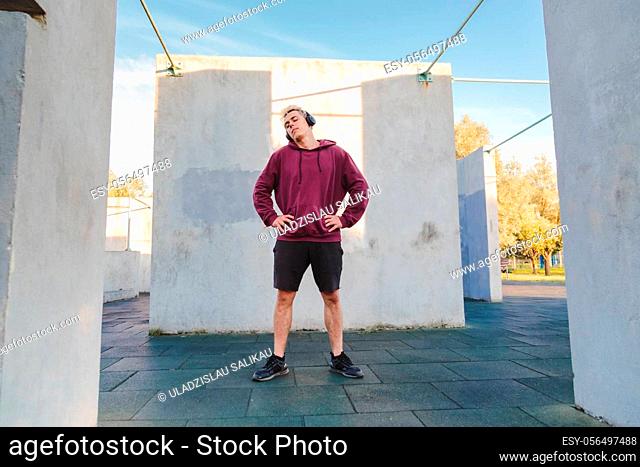 Sportsman warms up, doing neck rotation exercises and listening to music in headphones. Urban lifestyle photo
