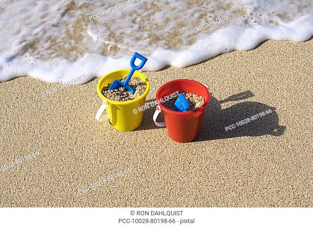 Two sets of brightly colored shovel and pails on a sandy beach