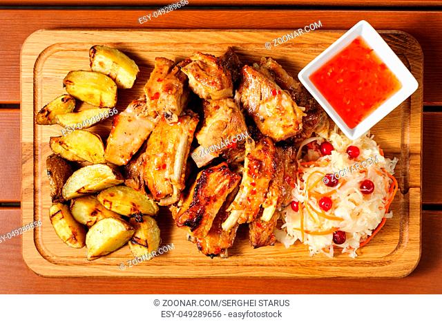 big wooden board with fried pork ribs, baked potato, hot sauce and sauerkraut, preferably served as companion for beer or other alcool drinks