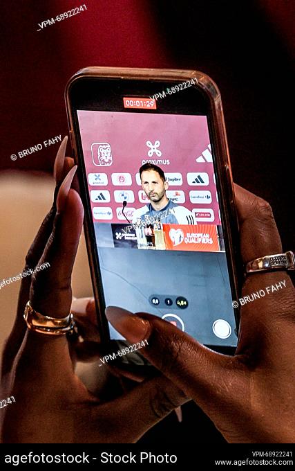 Belgium's head coach Domenico Tedesco is seen on the screen of a mobile phone held in her hands by a woman with very long fingernails and wearing several rings