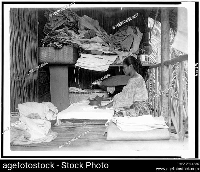 Javanese(?) woman sitting in room working with textiles at exhibit featuring foreign.., 1892. Creator: Frances Benjamin Johnston