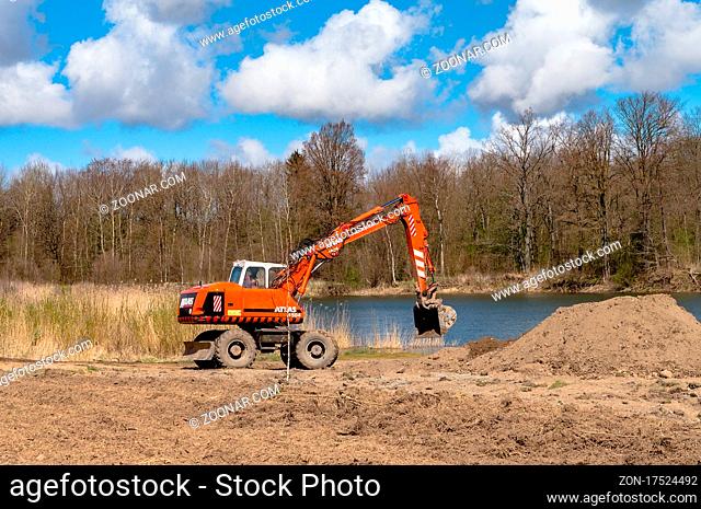 Kaliningrad Region, Russia, April 24, 2021. Excavator digging the ground. Improvement of the shoreline. Construction equipment on the shore of the pond
