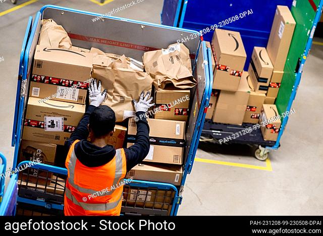 07 December 2023, Lower Saxony, Großenkneten: An employee distributes several parcels onto trolleys for shipping in the outgoing goods department at Amazon's...