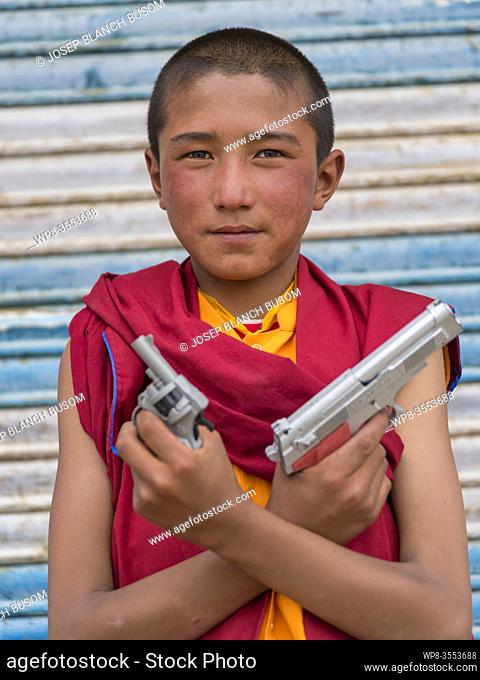 Young buddhist monk posing with toy pistols in Korzok, Ladakh, India