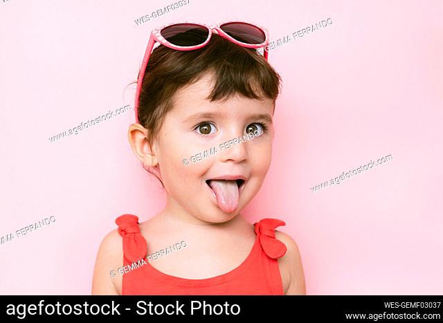 Portrait of little girl sticking out tongue in front of pink background