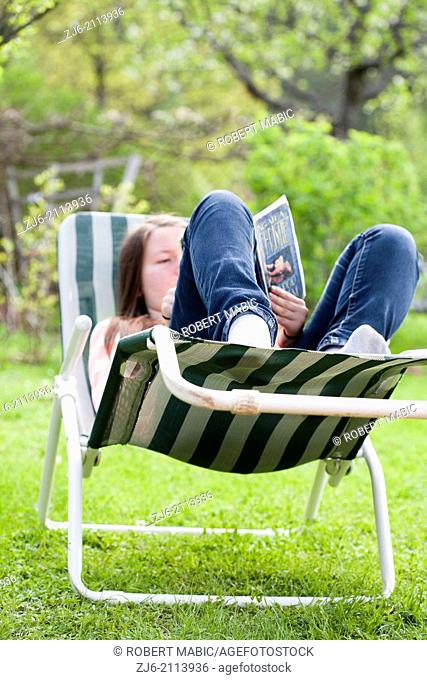 Teenage girl lying on a sun lounger and read a book outside in the garden