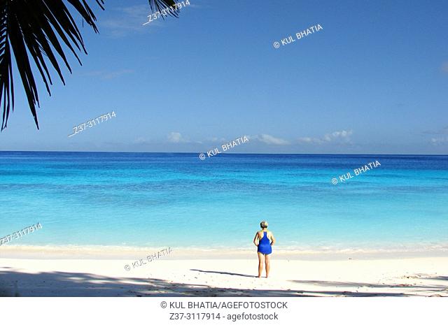 A blue-sky day at the beach in Mahe, the Seychelles. A woman in a blue bathing suit has the beach all to herself