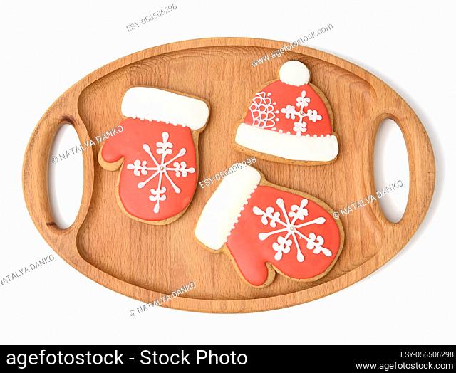 baked gingerbread in the shape of a mitten and covered with red icing, classic Christmas dessert on a wooden tray