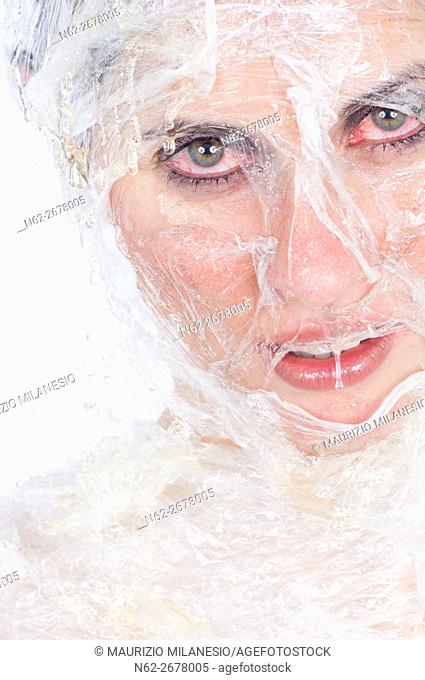 Face of a girl wrapped in plastic wrap, she is doing a beauty treatment with honey, her eyes are red with irritation