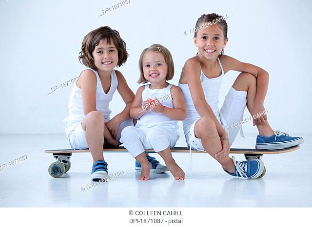 three young girls sitting on a long board