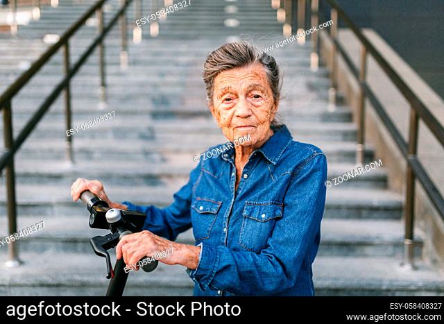 90 year old woman with gray hair, wrinkles, progressive and active uses modern electric transport scooter. Lady pensioner use eco friendly city vehicle