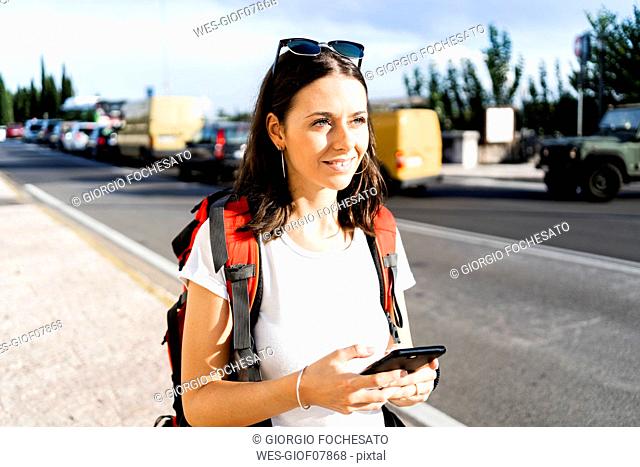 Young female backpacker with red backpack using smartphone in the city, Verona, Italy