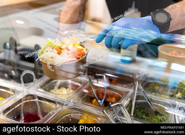 Chef with protective gloves preparing salad at food bar in restaurant