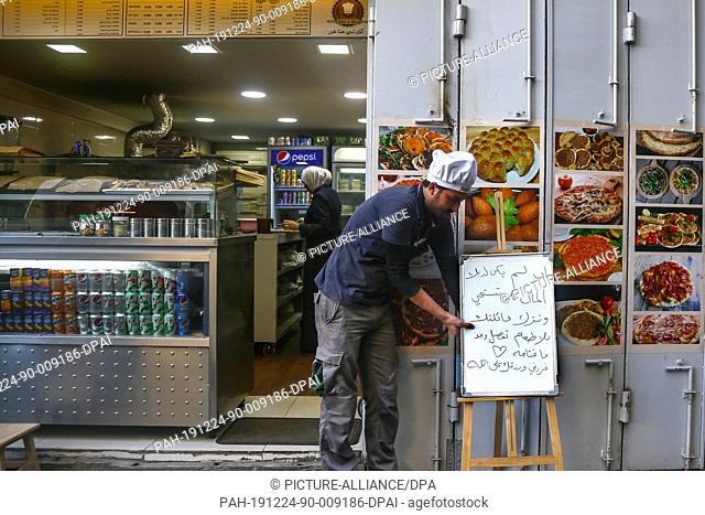 24 December 2019, Lebanon, Beirut: A shopkeeper adjusts a placard reading in Arabic ""If you do not have money, do not be ashamed and do not leave your family...
