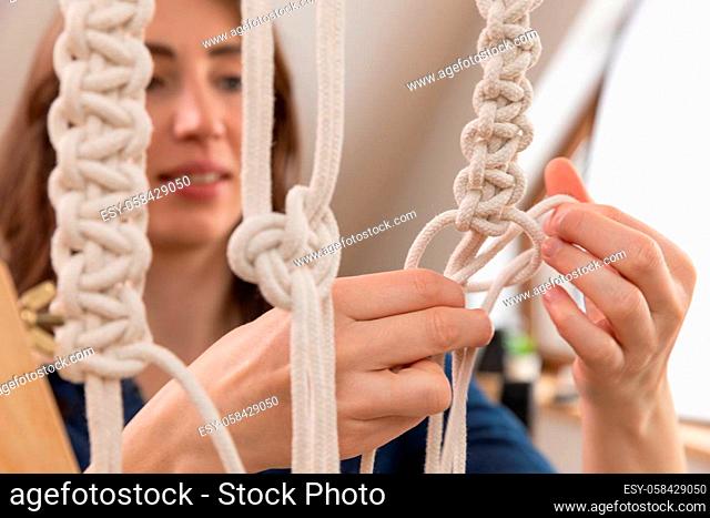 Woman relaxing and making macrame at home with different knots on a sunny day at home in attic. Stay at home hobbies