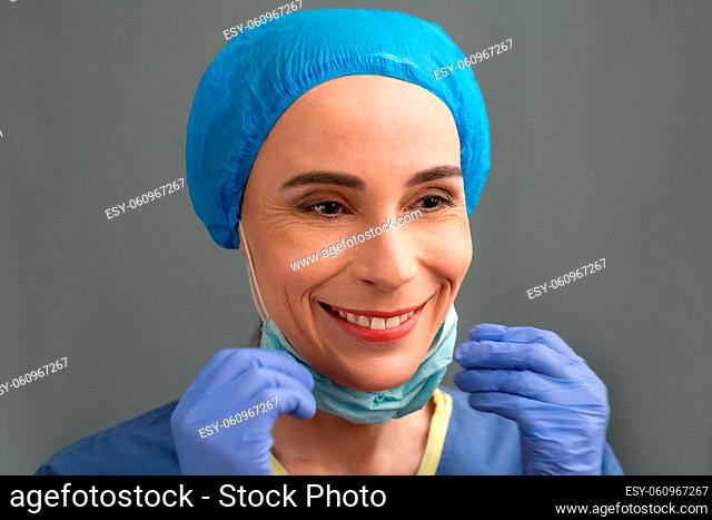Smiling Woman In Medical Clothes Rejoices At End Of The Coronavirus Epidemic, Caucasian Woman In Blue Medical Uniform And Gloves Toothy Smiles While Taking Off...